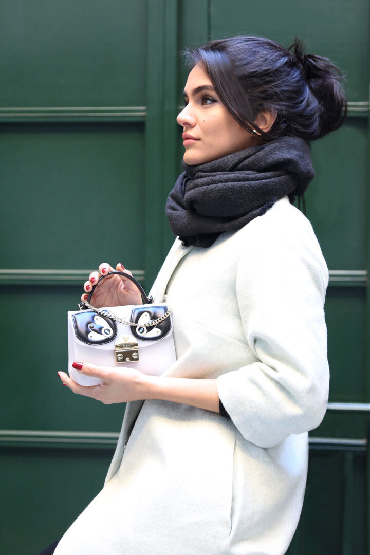 A woman wearing a white coat and black scarf, holding a Furla 978630 bag